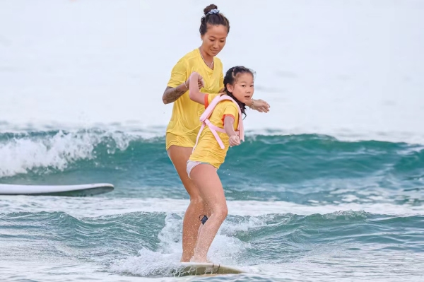 青少年兒童在沖浪教練的陪同下，在三亞市海棠區夏日水上運動嘉年華灣“乘風破浪”。三亞市體育旅游協會供圖